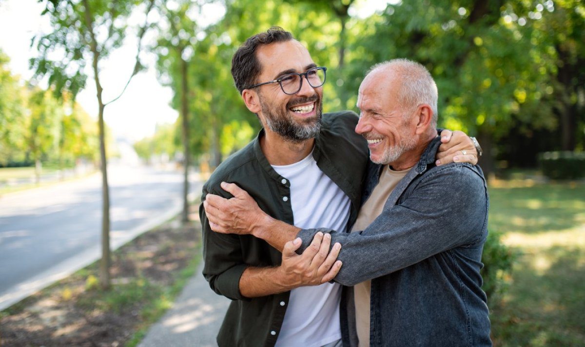 Senior man with his mature son embracing outdoors in park.