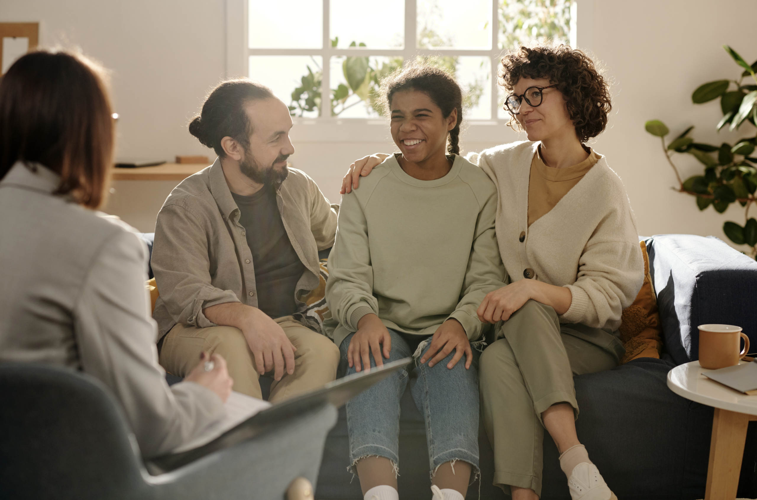 Foster parents sitting on sofa with adopted girl and talking to social worker during meeting at home Foster parents sitting on sofa with adopted girl and talking to social worker during meeting at home
